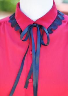 a woman wearing a pink shirt with blue ribbon around the neck and black lace on the collar