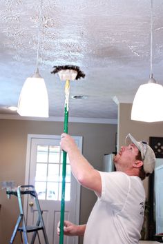 a man is painting the ceiling in his house with paint rollers and a brush