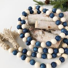 a white and blue beaded necklace next to a tree branch with pine cones on it