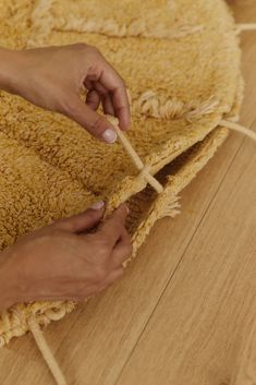 two hands on a rug that is laying on the floor and tying it with string