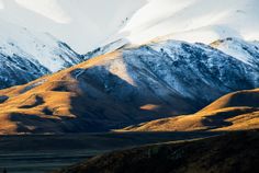 the mountains are covered in snow and brown grass