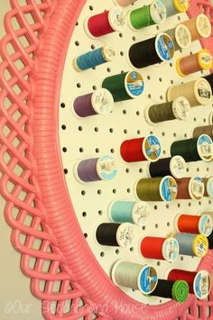 there are many spools of thread hanging on the wall behind this pink rack