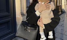 a woman holding a baby in her arms while walking down the street with a handbag