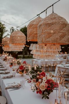 the tables are set up with white linens and red flowers on them, along with hanging chandeliers