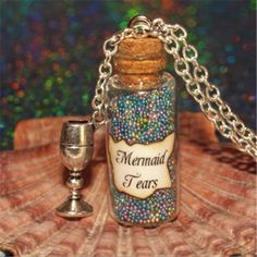 a bottle filled with lots of colorful beads next to a silver chalice charm on a chain