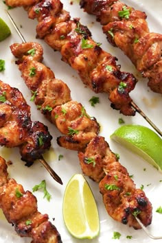 chicken skewers with lime wedges and cilantro on a white plate