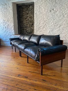 a black leather couch sitting on top of a hard wood floor next to a stone wall