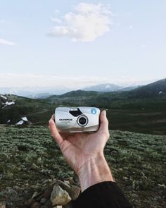 a person holding up a camera on top of a mountain