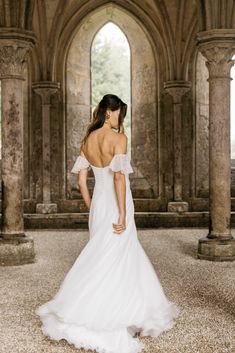 a woman in a white wedding dress is looking down at the ground with arches behind her