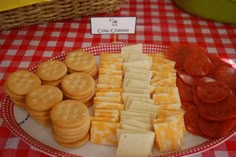 a plate full of crackers, cheese and pepperoni on a red checkered table cloth