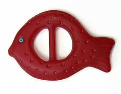 a red plastic fish shaped object on a white surface with holes in the center and blue eyes