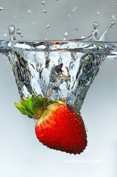 a strawberry falling into the water with splashes on its head and bottom, as if it were floating in air