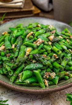 a bowl filled with green beans and nuts on top of a table next to a book