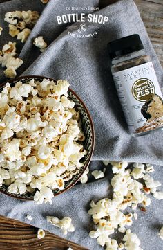 a bowl filled with popcorn next to a bottle of butter and seasoning on top of a table