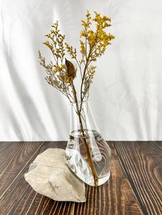 a glass vase filled with yellow flowers on top of a wooden table next to a rock