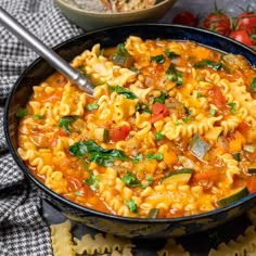 a bowl filled with pasta and vegetables on top of a table next to some bread