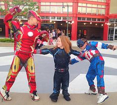 two children and an adult dressed as iron man in front of a building with people standing around