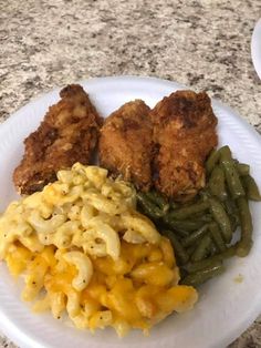 a white plate topped with macaroni and green beans next to fried chicken on top of it