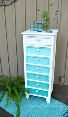 a blue and white dresser sitting on top of a wooden floor next to a plant