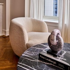 a marble table with a book on it in front of a chair and window sill