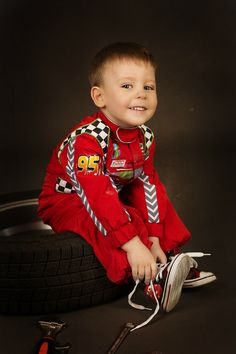 a young boy sitting on top of a tire next to wrenches and screwdrivers