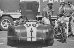 two men standing next to an old race car