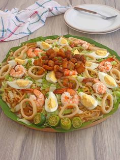 a large plate with noodles, shrimp and eggs on it sitting on a table next to a fork