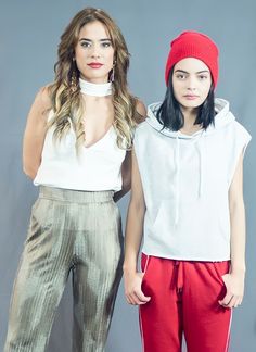 two women standing next to each other in front of a gray background wearing red pants