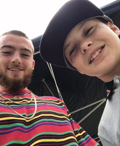 two young men standing next to each other with an umbrella in the back ground behind them