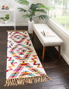 a white rug with multicolored designs on the floor next to a bench and potted plant