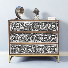 a black and white chest of drawers next to a silver vase on top of it