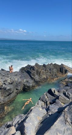 two people are swimming in the ocean near some rocks and water on a sunny day