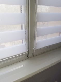 a window with white blinds and a phone hanging on it's side, in front of a window