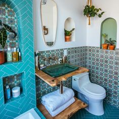 a bathroom with blue tiles and green tile on the walls, including a wooden shelf