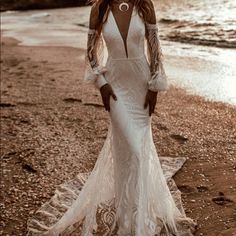 a woman standing on top of a beach next to the ocean wearing a white dress