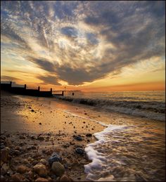 the sun is setting at the beach with waves coming in to shore and rocks on the sand