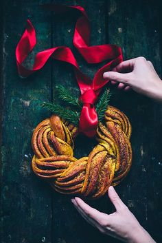 two hands holding a heart shaped pastry with red ribbon around it on top of a wooden table