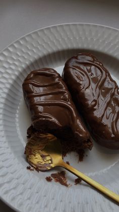 two pieces of chocolate cake on a white plate with a gold spoon next to it