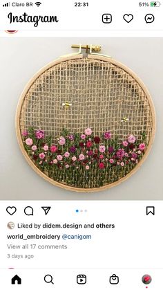 an embroidery project with pink flowers in the middle and green grass behind it on a white wall