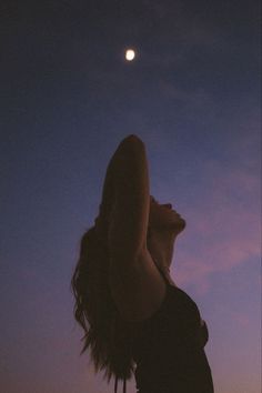 a woman standing in front of the moon with her arms up and head tilted to the side