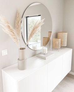 a white dresser topped with a round mirror next to a plant in a vase on top of it