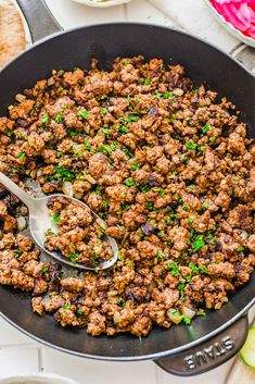 a skillet filled with meat and vegetables on top of a white table next to other dishes