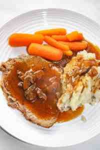 a white plate topped with meat and mashed potatoes covered in gravy next to carrots