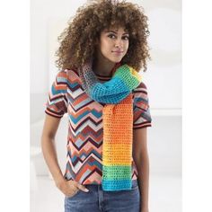 a woman with curly hair wearing a multicolored knitted scarf and standing in front of a white wall