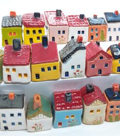 small ceramic houses are lined up against a white background, with one house painted red and the other yellow