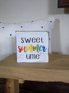 a wooden sign that says sweet summer time on the side of a table next to a pillow