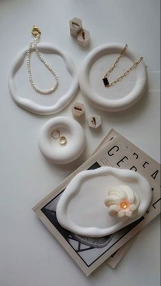 three pieces of jewelry sitting on top of a white table next to a magazine and necklaces