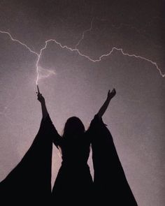 a woman with her hands up in the air while lightning strikes behind her and she is wearing black