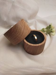 a wooden box with a ring in it on a white cloth next to a flower