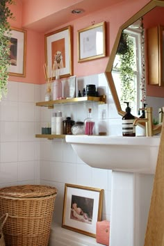 a bathroom with pink walls and pictures on the shelf above the sink, along with a wicker basket